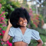 A joyful woman with an afro hairstyle posing in a vibrant garden in Mozambique.