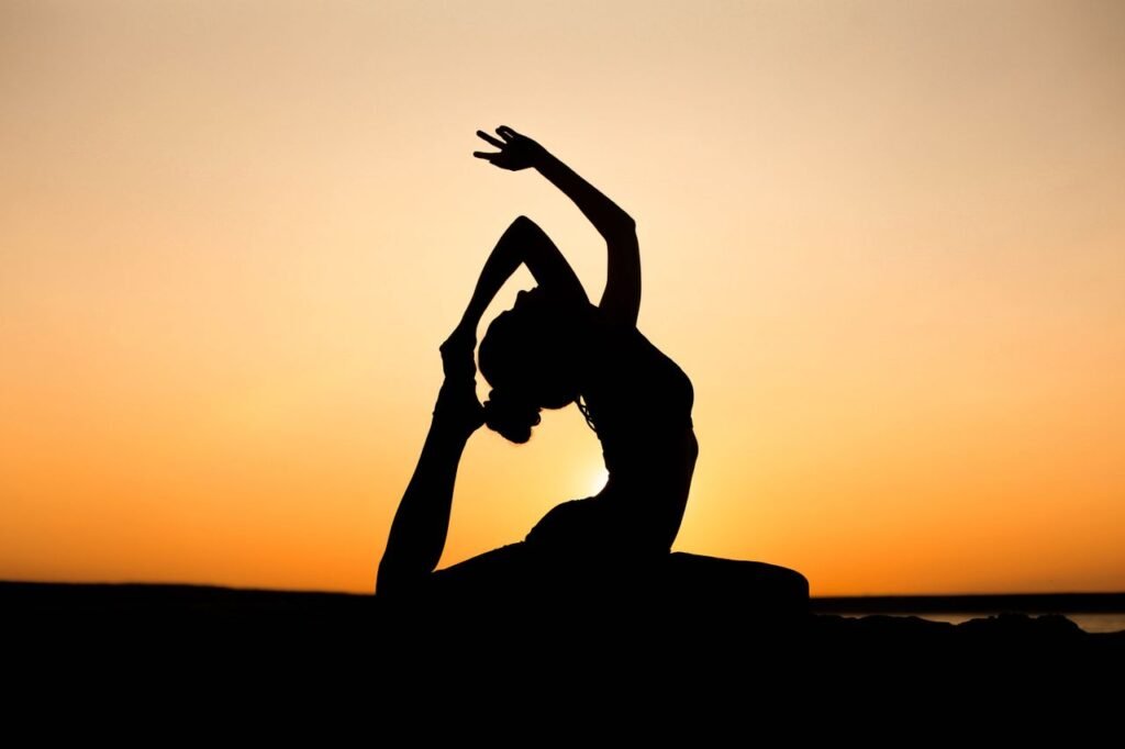 pexels-photo-11001515-11001515 A woman in a yoga pose silhouetted against a vibrant sunset sky, embodying peace and wellness.