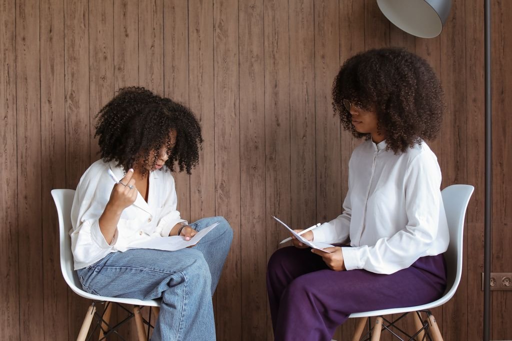 Photo by Polina Tankilevitch Two women engaged in a conversation while seated indoors, holding papers.