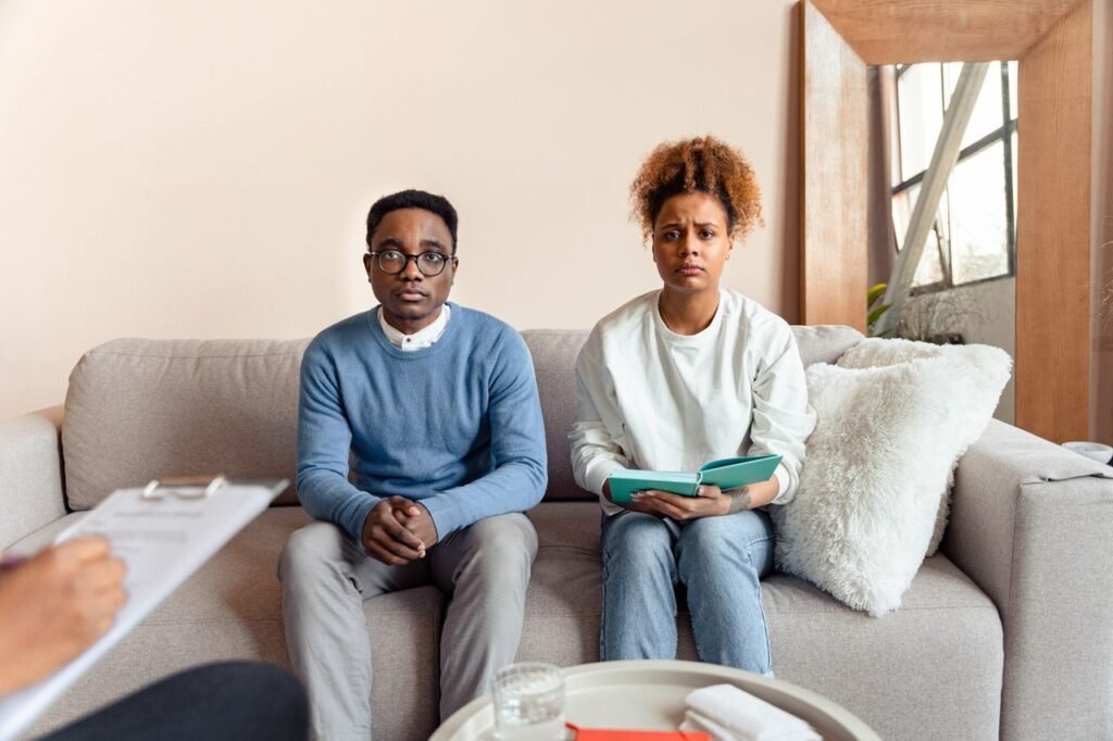 pexels-photo-7579105-7579105 A couple sits on a sofa during a therapy session, appearing concerned.