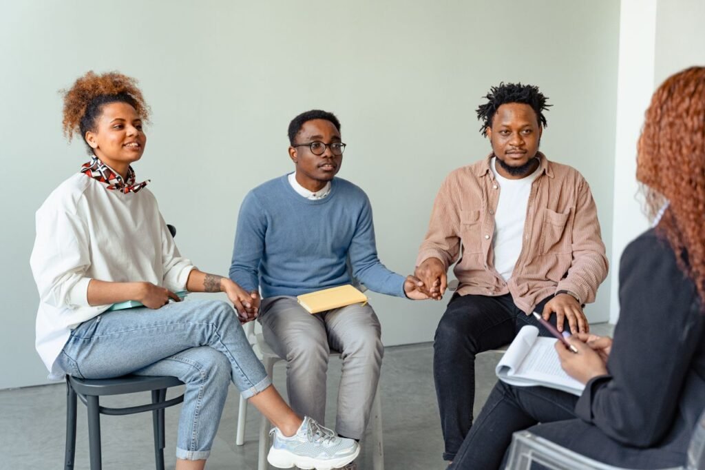 pexels-photo-7579306-7579306 A diverse group of adults in a supportive therapy session, holding hands indoors.